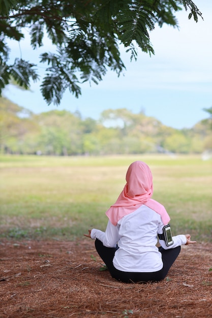 Muslim woman sitting on grass and enjoying yoga meditation