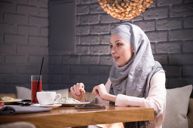식당 테이블에 앉아 있는 이슬람 여성