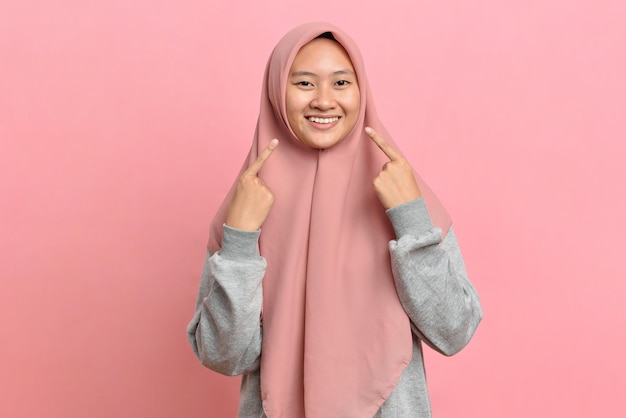 Foto donna musulmana sorridente allegra che mostra e indica con le dita i denti e la bocca