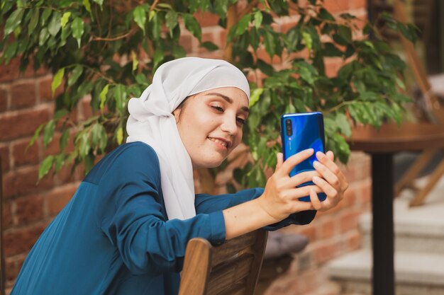 Donna musulmana che si fa selfie felice e bella ragazza con sciarpa si fa una foto usando lo smartphone