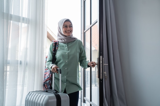 Muslim woman traveler opened the door entrance with her bag and suitcase