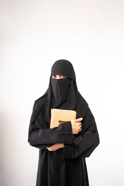 Muslim woman wearing a black hijab or niqab and long dress standing holding al quran looking at the