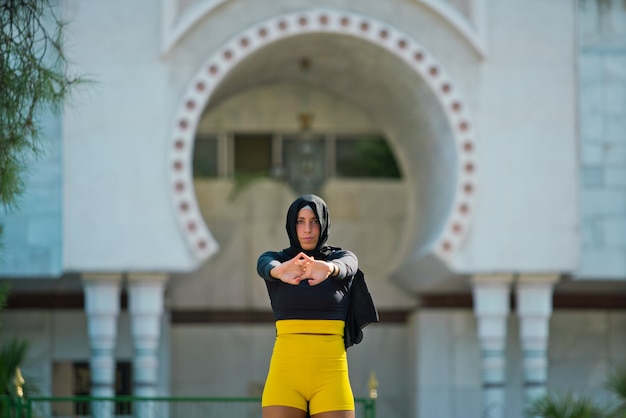 Muslim woman wearing a hijab and sportswear isolated with mosque background. Horizontal view of arabic woman training outdoors. Muslim women, religion and equality concept.