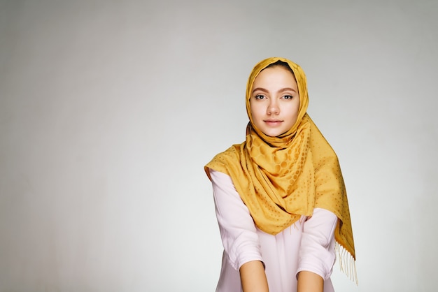 밝은 스튜디오에서 노란색 목도리에 진정 얼굴을 가진 무슬림 여성