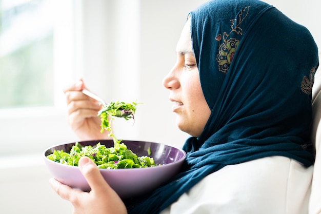 ヒジャブをかぶったイスラム教徒の女性が一人でグリーンサラダを食べる