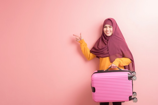 La donna musulmana con hijab sta tenendo i bagagli su fondo rosa, concetto di viaggio della gente