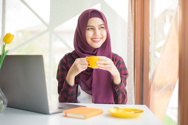 hijab와 무슬림 여성은 커피 숍에서 노트북 컴퓨터와 함께 일하고있다