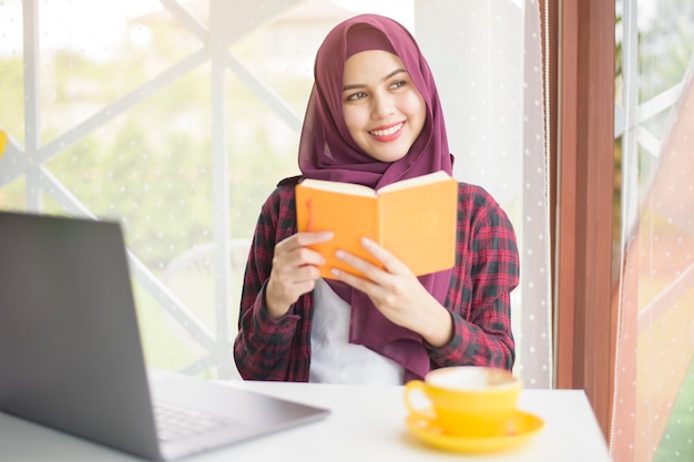 hijab와 무슬림 여성은 커피 숍에서 노트북 컴퓨터와 함께 일하고있다