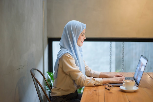 ヒジャーブとイスラム教徒の女性はコーヒーショップでラップトップコンピューターで働いています。