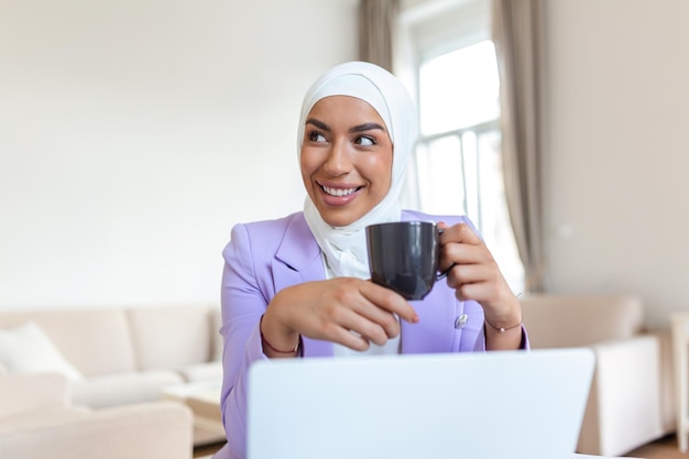 Muslim woman working with computer Arab Young business woman sitting at her desk at home working on a laptop computer and drinking coffee or tea Muslim woman working at a home and using computer