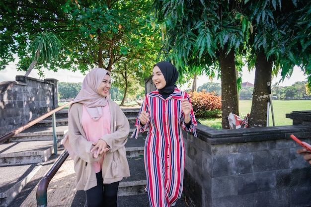 Muslim women in hijabs outdoors on sunny day with friend happy and laugh while walking outdoor