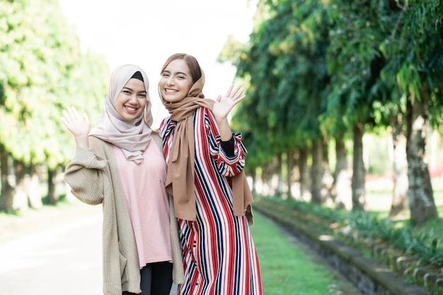 Muslim women in hijabs outdoors on sunny day with friend happy wave their hand to camera