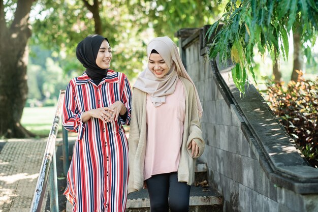 Muslim women in hijabs outdoors on sunny day with friend happy