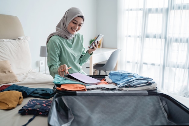 Muslim women wearing hijab preparing suitcase while making a\
list