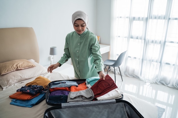 Muslim women wearing hijabs prepare clothes to be put in a suitcase