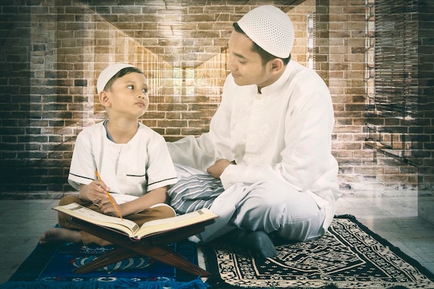 Muslim young man teaching his son to read Quran