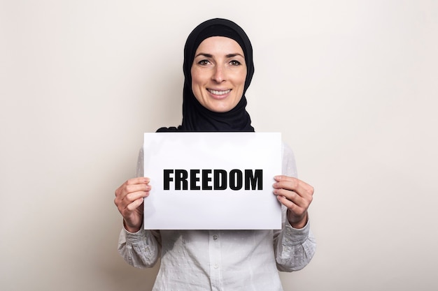 ヒジャーブで笑顔のイスラム教徒の若い女性は、テキストFREEDOMのバナーを保持しています