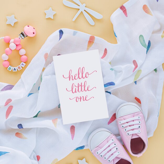 Muslin swaddle blanket with card Hello little one and baby slippers, toys on yellow background.  Set of  newborn accessories. Flat lay, top view