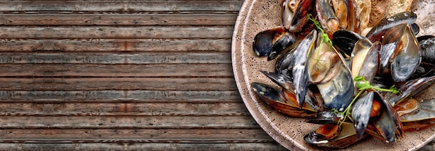 Mussel molluscs in creamy cheese sauce with toasts, on a plate, on wooden background with copy space. Horizontal