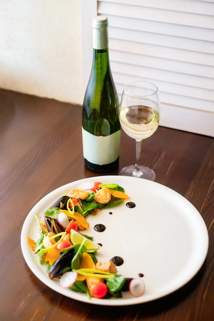 Mussel salad on a white plate with glass and bottle of wine\
concept of a beautiful dish serving for a restaurant