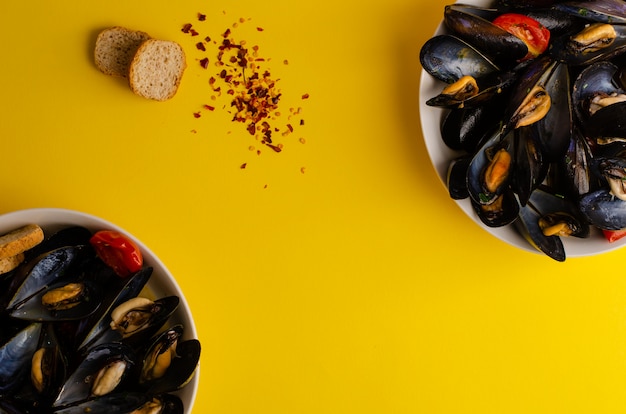 Mussel soup steamed in wine with tomatoes, hot peppers and crisp bread on yellow background