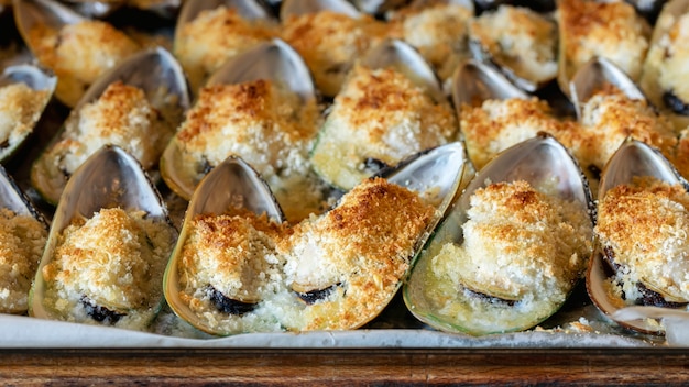 Mussels baked with parmesan, bread crumb and herb butter . Food background. Mediterranean cuisine. Concept for a tasty and healthy meal. Close up.