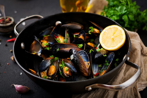 Mussels cooked in wine sauce with herbs in a frying pan on a black table.