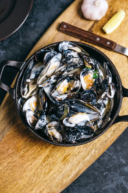 Mussels in a creamy garlic sauce in a black metal plate on a wooden board.