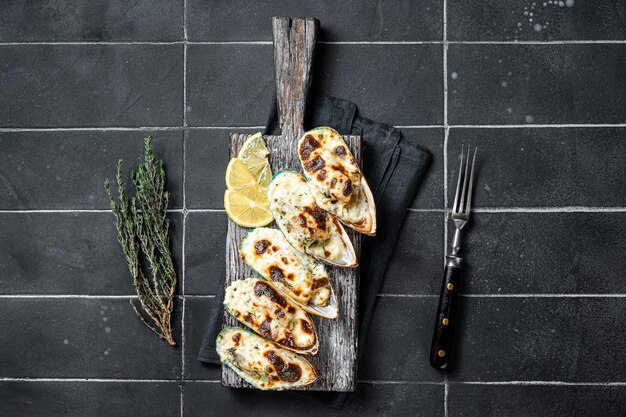 Mussels in roquefort cheese sauce in shells on wooden board black background top view