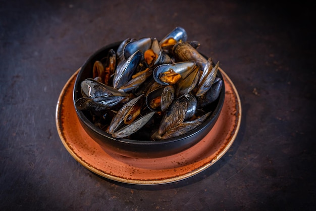 Mussels in sauce on a black background in an orange plate