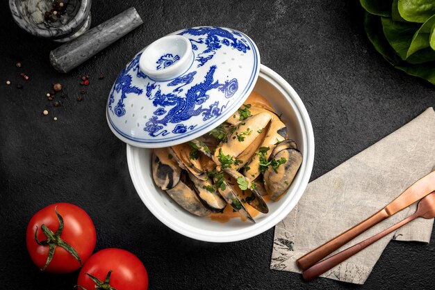 Mussels in sauce in a ceramic dish on a dark decorated background