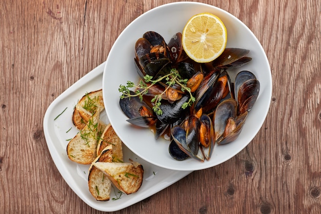 Mussels on a white plate on a wooden board