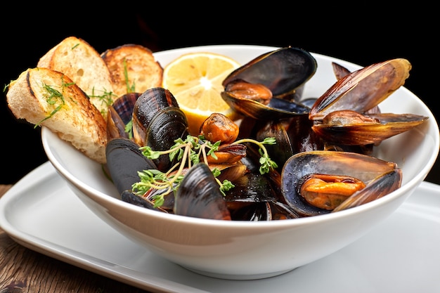 Mussels on a white plate on a wooden board