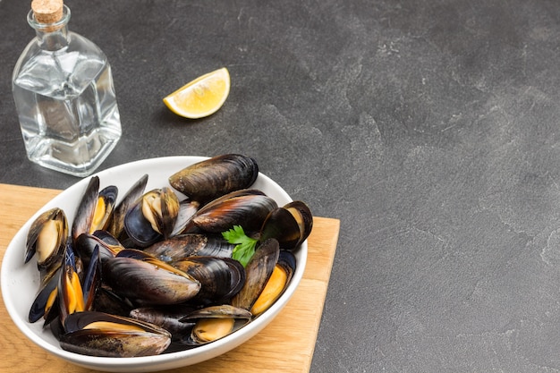 Mussels with open shells in white bowl on cutting board. bottled water and sauce. top view.