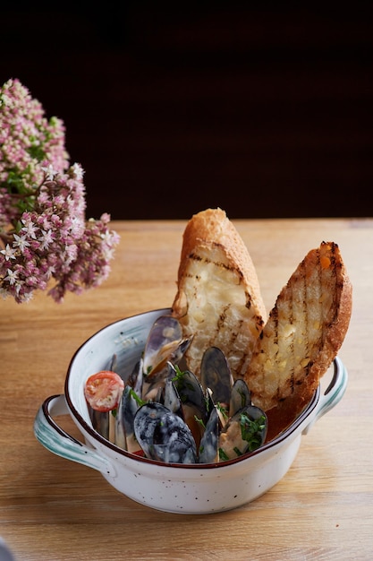 写真 プレートにソースを添えたムール貝、焼きたてのパン、木製のテーブルに花を添えてクローズアップ。レストランのコンセプト