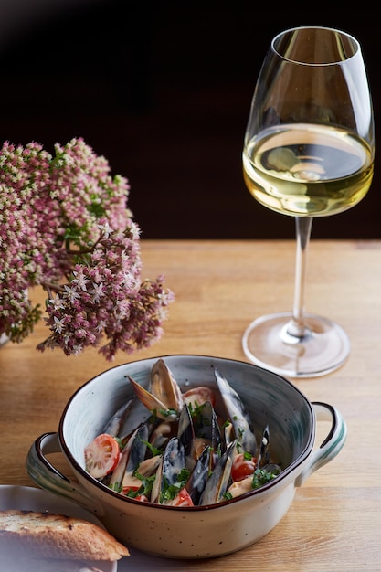 Foto cozze con salsa in piatto su tavola di legno con bicchiere di vino bianco e fiori vicino e sfondo scuro. concetto di ristorante