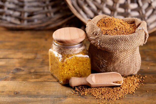 Mustard seeds in bag and Dijon mustard in glass jar on wooden background