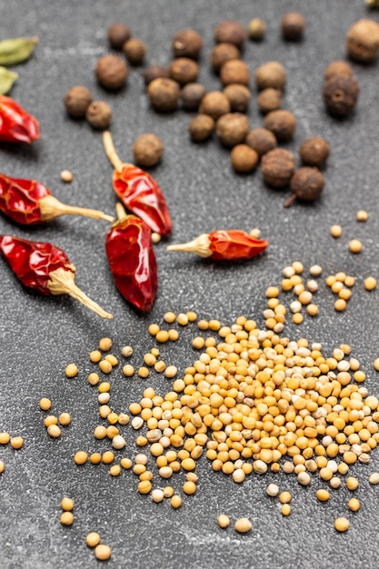 Mustard seeds dry red pepper pods and allspice on table Top view Black background