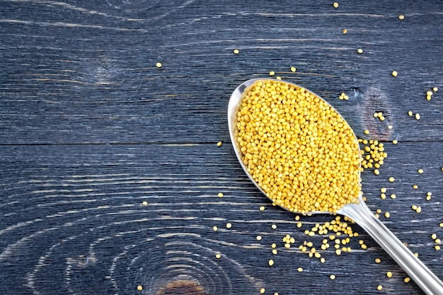 Mustard seeds in a metal spoon on the background of a wooden board from above