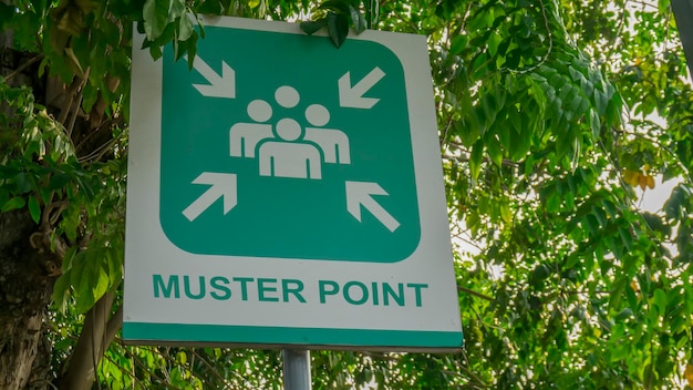 Muster point signboard with green tree leaves background
