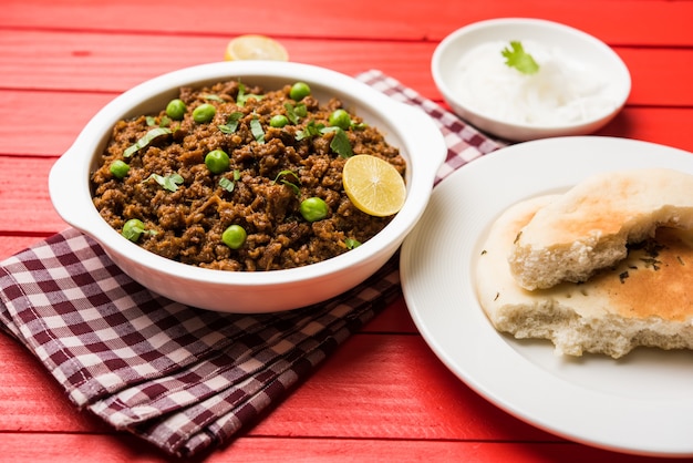 Mutton Kheema Pav OR Indian Spicy Minced Meat served with bread OR kulcha, garnished with green peas. Moody background. Selective focus
