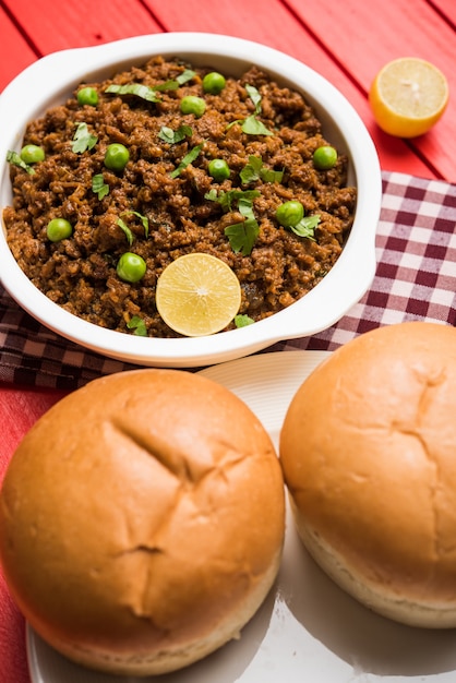 Mutton Kheema Pav OR Indian Spicy Minced Meat served with bread OR kulcha, garnished with green peas. Moody background. Selective focus