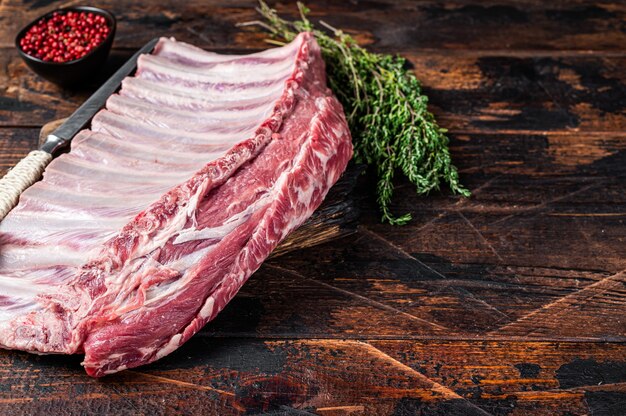 Mutton lamb ribs rack on wooden cutting board. Dark wooden background. Top view. Copy space.