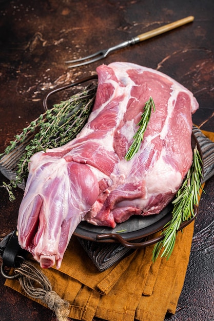 Mutton lamb whole shoulder raw meat in a steel tray with herbs Dark background Top view