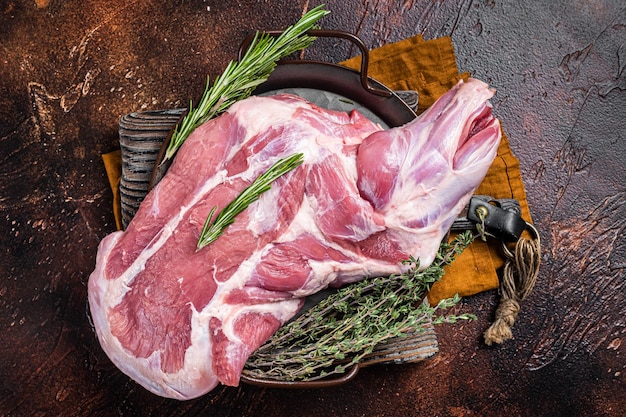 Mutton lamb whole shoulder raw meat in a steel tray with herbs Dark background Top view