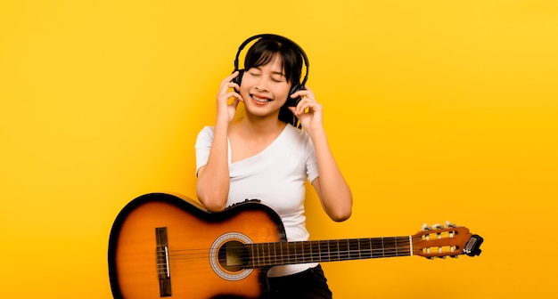 Muziek en ontspanning concept mooie aziatische vrouw in koptelefoon luisteren naar muziek en dansen op gele achtergrond gelukkig in het leven