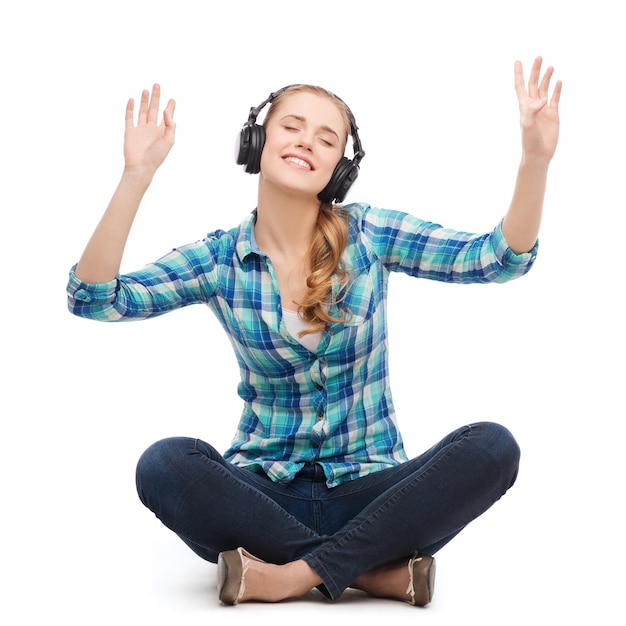 muziek- en technologieconcept - glimlachende jonge vrouw die op de vloer zit en naar muziek luistert met een koptelefoon