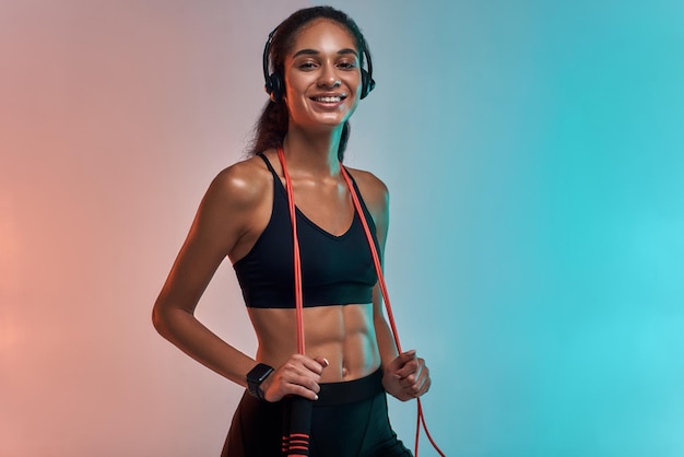 Foto muziek is mijn motivatie sportieve jonge vrouw in koptelefoon met springtouw op schouders en