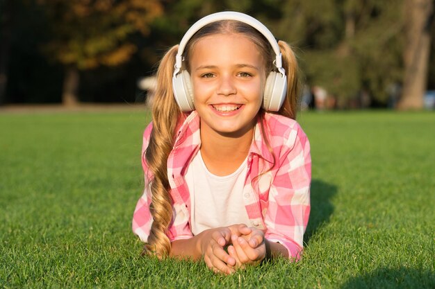 Muziek om u te helpen rusten Gelukkig kind luistert naar muziek liggend op groen gras Plezier en amusement Vrijetijdsactiviteiten Modern leven en technologie Frisse lucht ontspannen Zomervakantie