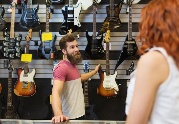 muziek, verkoop, mensen, muziekinstrumenten en entertainmentconcept - assistent die elektrische gitaar toont aan klant bij muziekwinkel